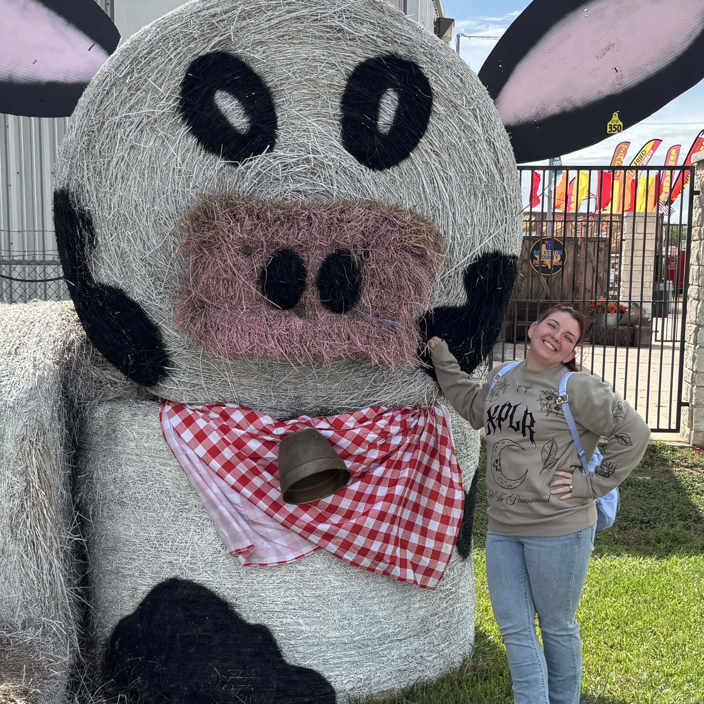 Jackie stands with a cow sculpture made of hay.